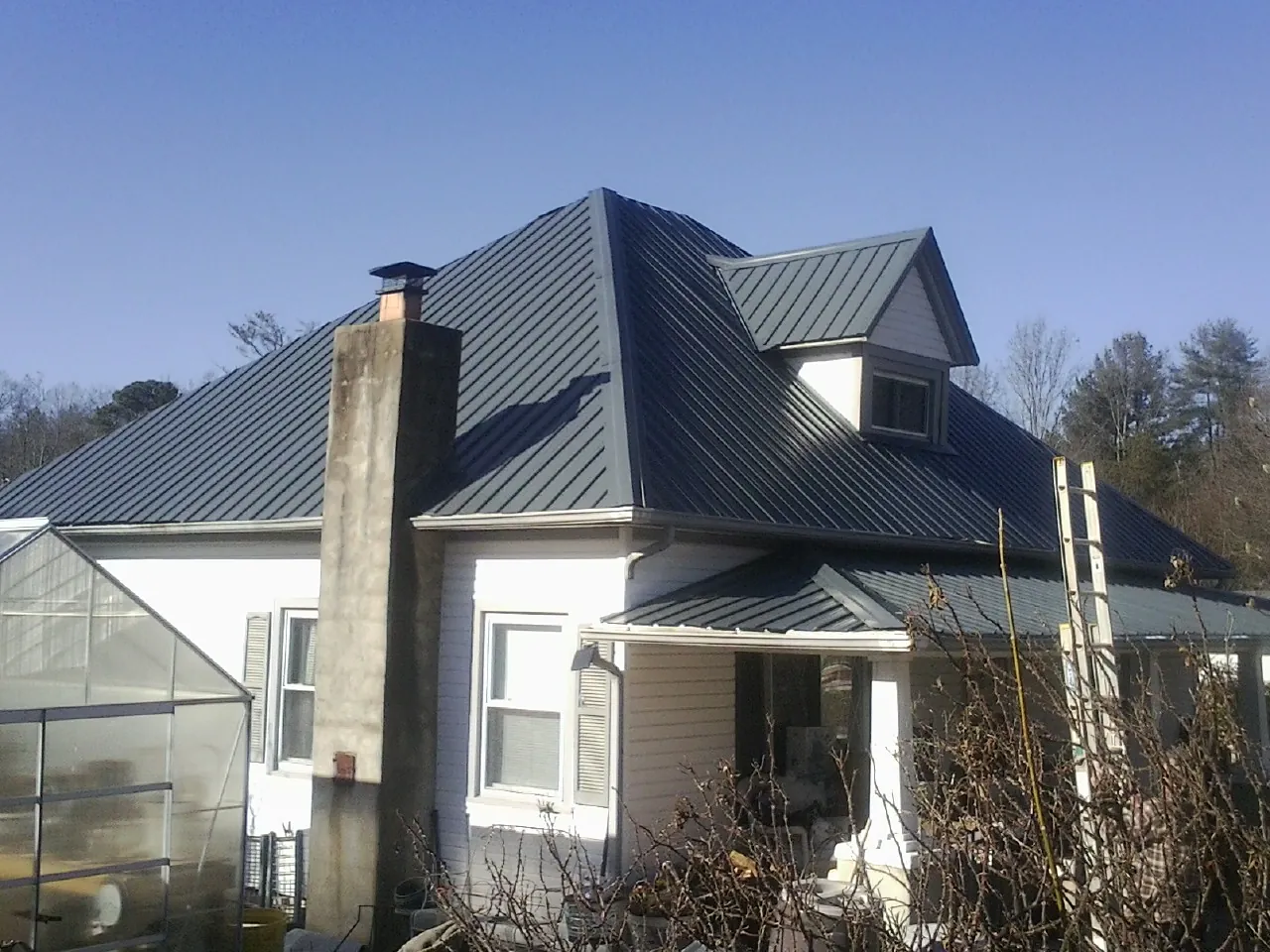 Dark blue standing seam metal roof on a white farmhouse with dormer — Slate & Tile Roof Repair by Roofing Brothers in Merry Hill