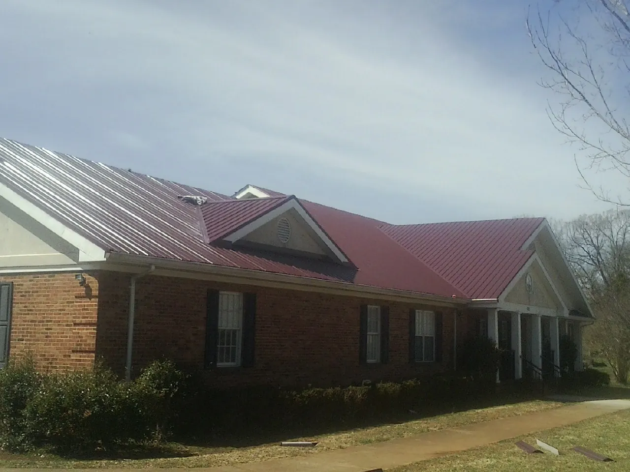 Red metal roof with gabled entries on a long brick building, from a Hail Damage Roof Repair job in Merry Hill