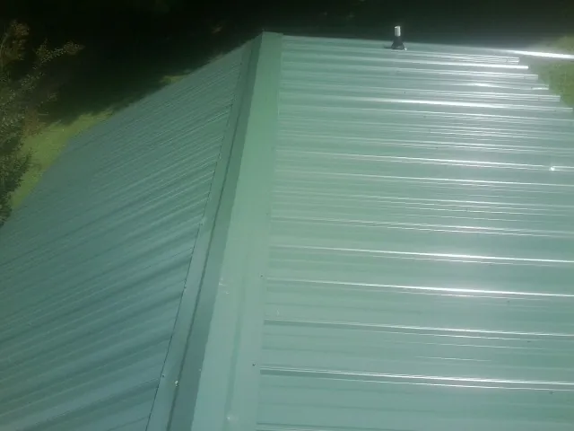 New green metal panels meeting at the ridge of a roof — Flat Roof Repair work by our crew in Merry Hill
