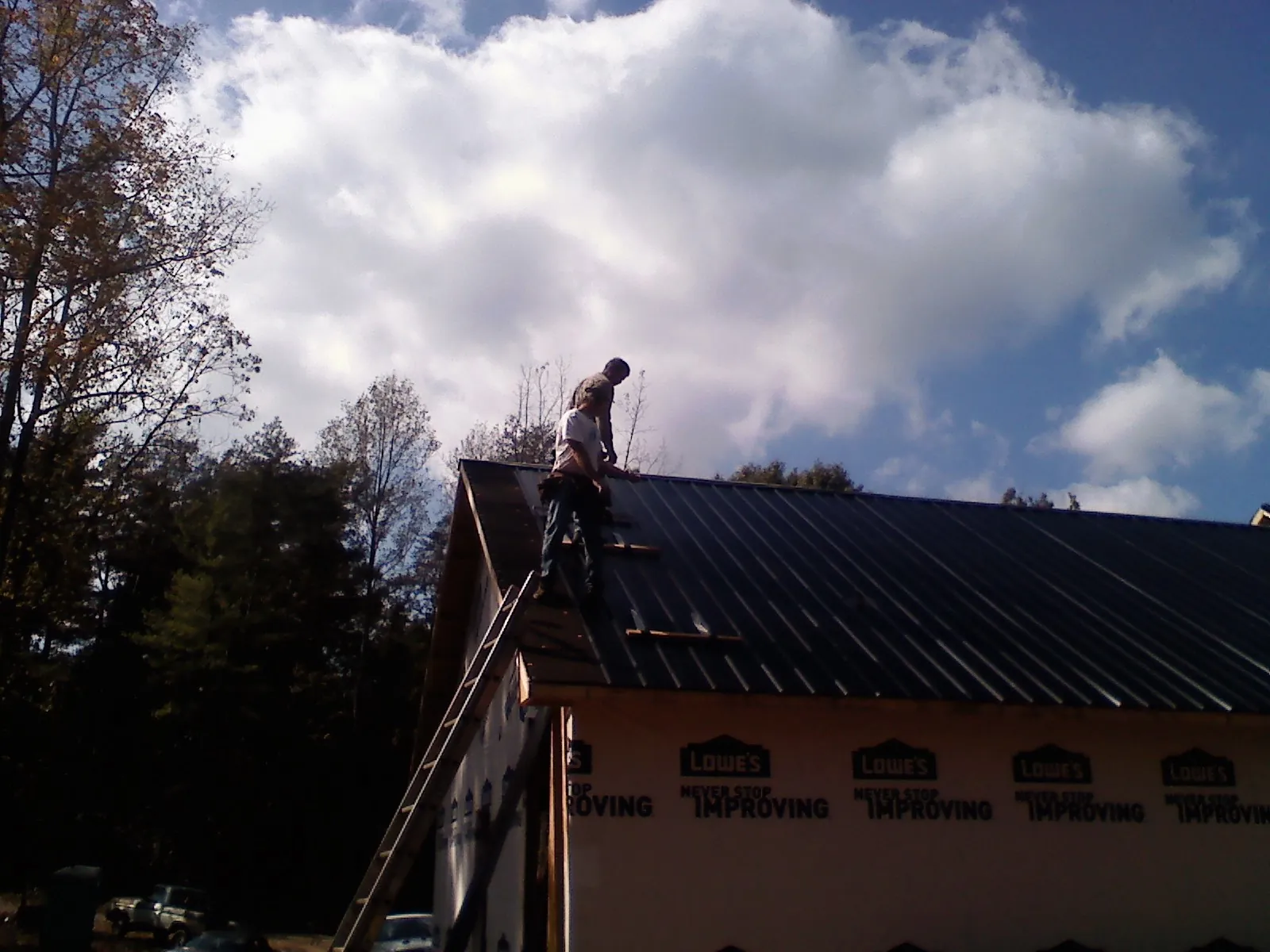 Roofer fastening dark metal panels high against a cloudy sky, from a Roof Inspection job in Merry Hill