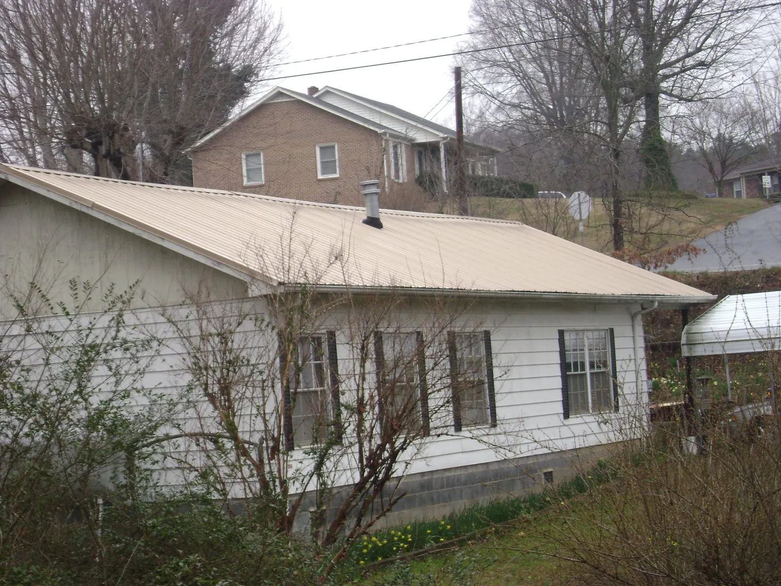 Tan metal roof on a white sided house set into a hillside — Commercial Roofing by Roofing Brothers in Merry Hill