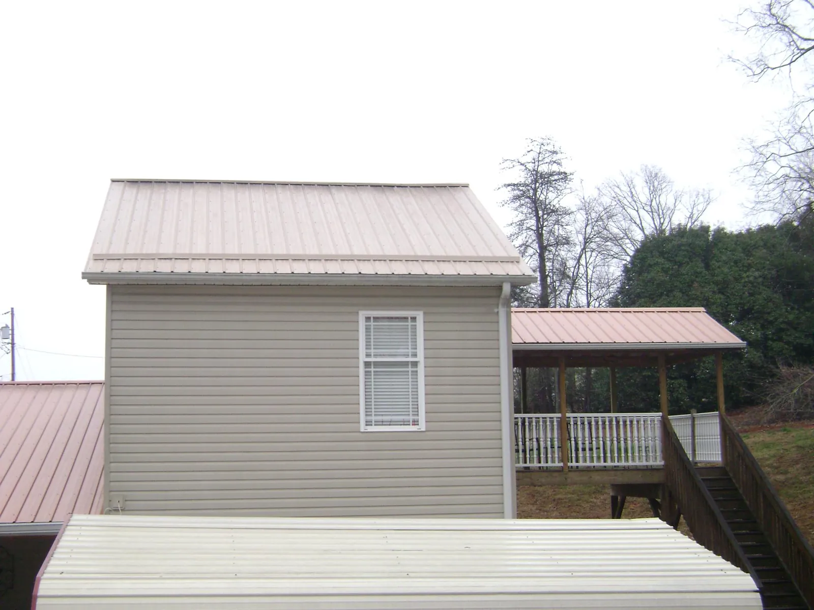 Tan metal roofs on a two story addition and attached porch, from a Roof Replacement job in Merry Hill